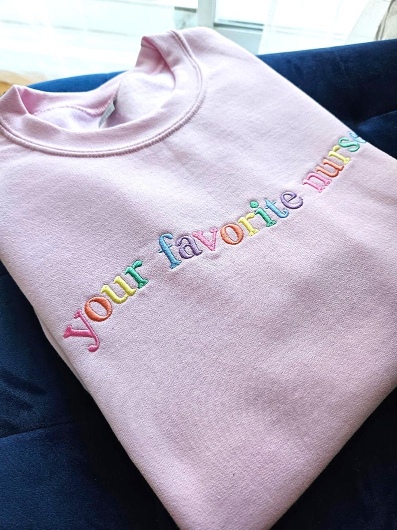 May include: A pink sweatshirt with the text "your favorite nurse" embroidered in rainbow colors.
