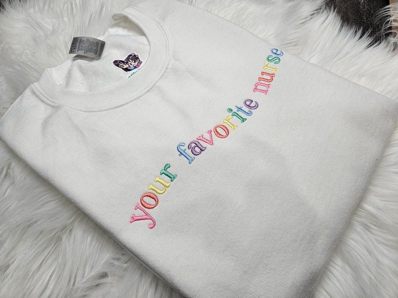 May include: White t-shirt with the text "Your favorite nurse" embroidered in rainbow colors.