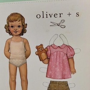 May include: A paper doll set featuring a girl with brown hair and a pink dress, brown shorts, and a teddy bear puppet. The set includes a pair of scissors and the text "oliver + s PUPPET SHOW TUNIC".