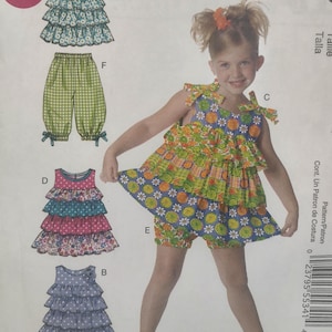 May include: A young girl models a colorful children's clothing pattern. The pattern includes a tiered dress, ruffled top, and shorts. The designs feature floral and polka dot patterns, with the word "EASY" in a pink circle.