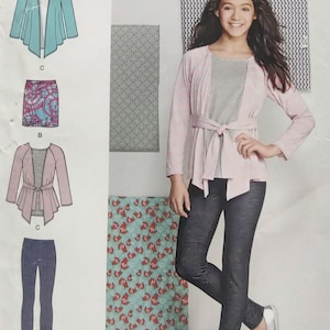 May include: A young person wearing a light pink cardigan with a gray top and dark gray pants. The cardigan has a tie at the waist. The image also shows a pattern for a skirt, pants, and a cardigan.