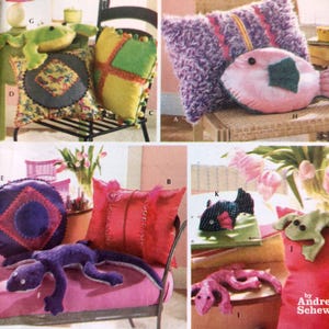 May include: A collection of decorative pillows and stuffed animals in various shapes and colors. Pillows include a purple shaggy pillow with pink stripes, a pink fish pillow, and a red pillow with vertical stitching. Stuffed animals include a green frog and a purple lizard.