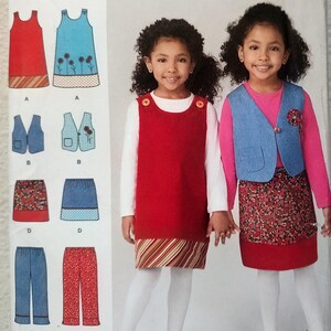 May include: A sewing pattern envelope featuring illustrations of children's clothing including a red jumper dress with a striped hem, a blue vest, a floral skirt, and pants. Two children are shown wearing the red jumper and the blue vest ensemble.