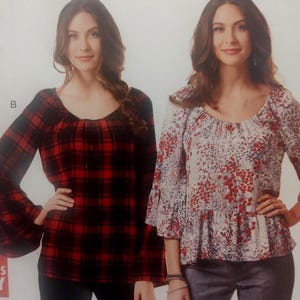 May include: Two long-sleeved tops with scoop necklines. The top on the left features a red and black plaid pattern with wide bell sleeves. The top on the right features a white base with a red and blue floral print, three-quarter sleeves, and a ruffled hem.