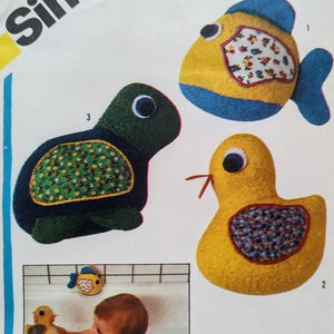 May include: A sewing pattern illustration featuring three stuffed animal toys: a yellow and blue fish with a floral patch, a dark green turtle with a green floral shell, and a yellow duck with a purple floral patch, plus a photo of the toys in a tub.
