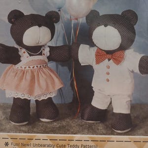 May include: Two handmade teddy bears, one in a dress and the other in a suit. The bear on the left wears a pink and white striped dress with a white lace trim and a pearl necklace. The bear on the right wears a white suit with a red bow tie.