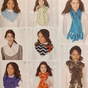 May include: A collection of eight distinct fleece scarves displayed in a grid. Styles include a light blue buttoned cowl, a green polka dot ruffled scarf, a blue braided fringe scarf, a white floral scarf, a chevron print cowl, a purple ruffled scarf, an orange floral scarf, and a leopard print ruffled scarf.