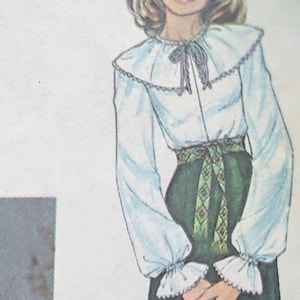May include: A fashion illustration of a long-sleeved white blouse with a large ruffled collar, a dark gray tie at the neck, and gathered cuffs. The blouse is paired with a dark green skirt featuring a decorative green and brown patterned sash.