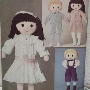May include: A vintage sewing pattern featuring several fabric dolls. The main doll wears a white dress with a pink ribbon. Other dolls are dressed in a suit, a pink dress, and purple overalls. The dolls have yarn hair and painted faces.