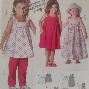May include: A sewing pattern featuring three girls' dresses and a pair of pants. The dresses are in pink and white, with polka dots and heart patterns. The pattern includes illustrations of the garments and the text "NO RETURNS, EXCHANGES OF REFUNDS ON FABRIC DE".