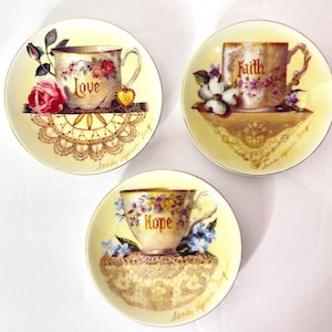 May include: A white ceramic mug with a black handle and the text "But first, coffee" in a black, handwritten-style font. The mug is on a white surface.