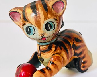 Juguete de cuerda vintage de hojalata litografiada de mediados de siglo con forma de gato atigrado y pelota - Japón - Tal cual, sin llave