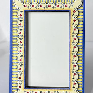 May include: A rectangular picture frame with a blue border and a yellow and blue striped background. The frame has a scalloped edge with a cherry design. The inner frame is black, and the center is white.