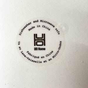 Puede incluir: Primer plano de una superficie blanca con una pegatina circular. La pegatina dice "Dishwasher and Microwave safe Made in China" y "UO Home". Tambi&eacute;n hay texto en franc&eacute;s: "Fabriqu&eacute; en Chine" y "Lave-Vaisselle et au Micro-Ondes".