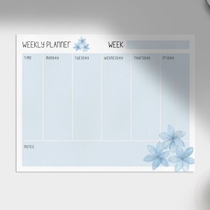 Puede incluir: Un planificador semanal con un fondo azul claro y un diseño floral en la esquina inferior derecha. El planificador tiene secciones para cada día de la semana, de lunes a viernes, y una sección de notas en la parte inferior.