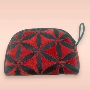 May include: A half-moon shaped pouch with a black zipper and a small handle. The pouch is decorated with a floral pattern in red and black leather. The red leather has a textured appearance.
