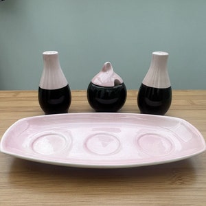 May include: A pink and black ceramic salt and pepper shaker set with a matching sugar bowl. The set is on a pink tray with three indentations.