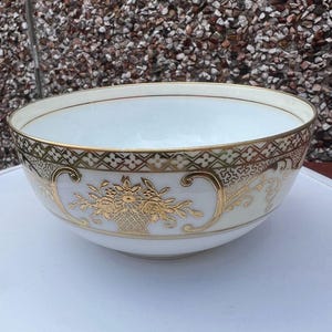 May include: A large white porcelain bowl with a gold rim and intricate gold floral designs. The bowl has a scalloped edge and is perfect for serving fruit or salad.
