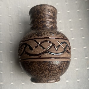 Puede incluir: Un pequeño jarrón de cerámica marrón con un diseño decorativo en relieve marrón y rojo alrededor del centro. El jarrón tiene un esmalte marrón moteado.
