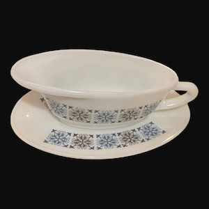May include: White ceramic gravy boat with a blue and brown geometric pattern. The boat is on a matching saucer.