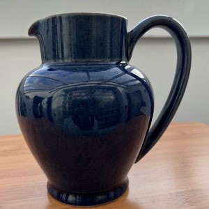 Peut inclure: Un pichet en céramique bleu foncé avec un glaçage moucheté et un corps arrondi. Le pichet a une large ouverture et une anse.