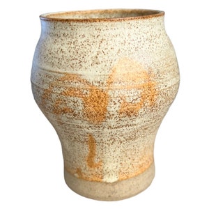 May include: A ceramic vase with a speckled white glaze and brown accents. The vase has a rounded body and a flared lip.