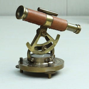 Peut inclure: Un télescope nautique vintage en laiton et cuir. Le télescope a une poignée en cuir marron et est monté sur une base en laiton avec une boussole et une échelle de degrés. La base a trois pieds réglables.