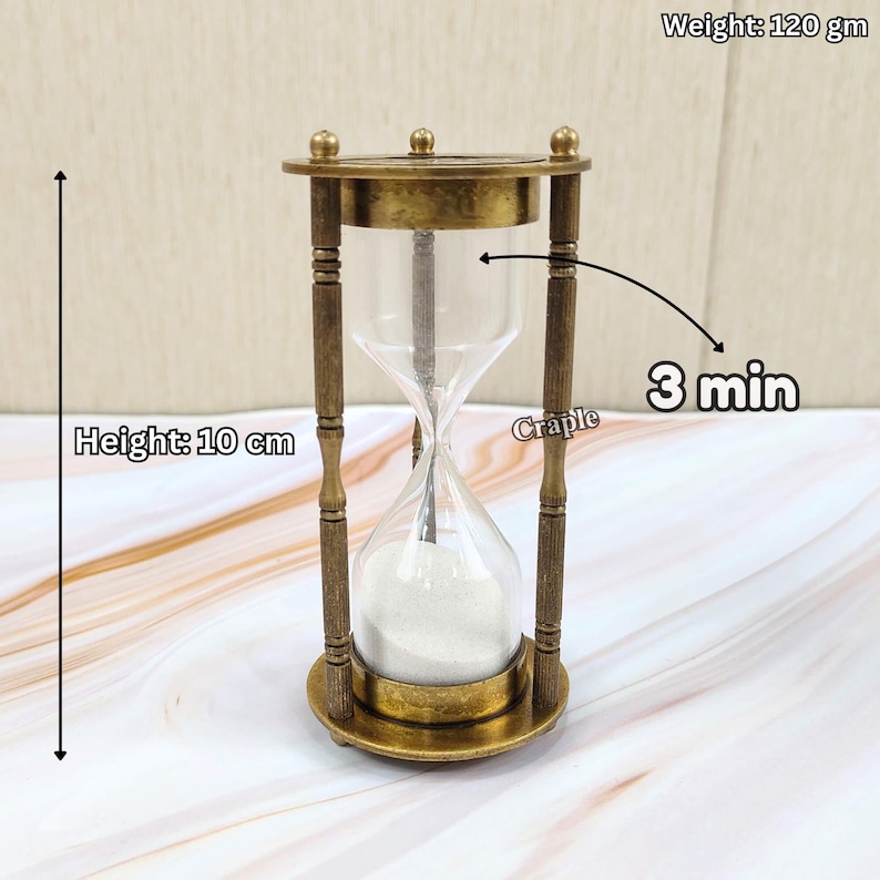 May include: A vintage-style hourglass with a brass frame and clear glass. The hourglass is 10 cm tall and weighs 120 grams. The sand timer is designed to measure 3 minutes. The hourglass has a decorative design.