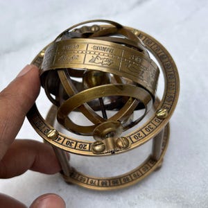 May include: A brass armillary sphere with zodiac symbols and degree markings. The sphere has multiple rotating rings and a central globe. The text "TAURUS" is visible on one of the rings. The sphere is a decorative item.
