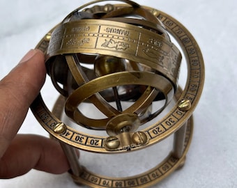 Op de afbeelding: Een messing armillairsfeer met dierenriemtekens en gradenmarkeringen. De sfeer heeft meerdere roterende ringen en een centrale globe. De tekst "TAURUS" is zichtbaar. Een decoratief astronomisch instrument.