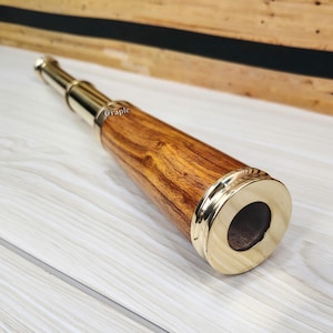 May include: A vintage-style brass and wood telescope. The telescope has a wooden body with brass accents on the ends and the eyepiece. The wood has a warm, natural grain. The telescope is designed to be handheld.