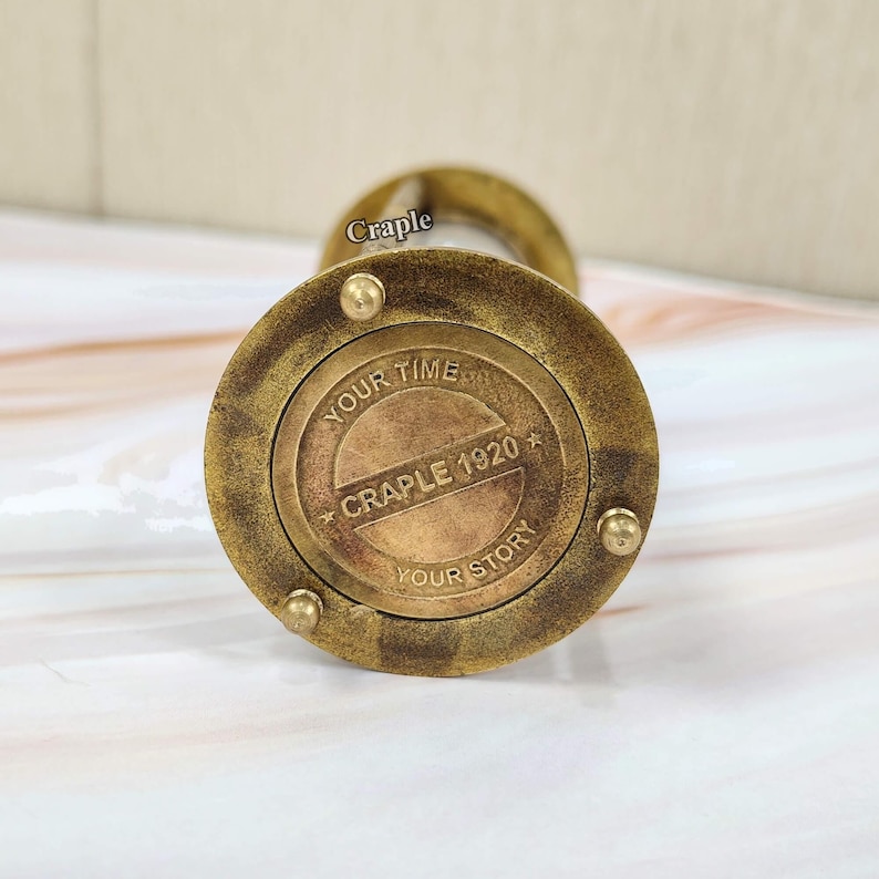 May include: A vintage brass hourglass with the text "YOUR TIME YOUR STORY CRAPLE 1920" on the base. The hourglass has a classic design with a circular base and top, and a narrow center.