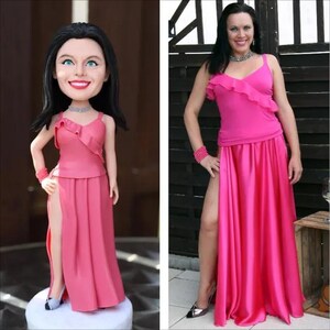 May include: A custom bobblehead figurine featuring a person with long dark hair wearing a bright pink sleeveless top with a ruffled neckline and a matching floor-length skirt with a high side slit, paired with a silver necklace and bracelet.