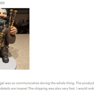 May include: A figurine of a bearded character wearing a brown tunic and dark trousers, holding a set of bagpipes with gold-colored accents. The figure has long dark hair, a full beard, and stands on a circular base, featuring detailed textures.