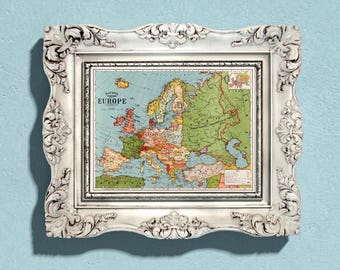 May include: A vintage map of Europe in a white ornate frame. The map is printed on paper with a light blue background and shows the countries of Europe in different colors. The map is titled "Bacon's Map of Europe".