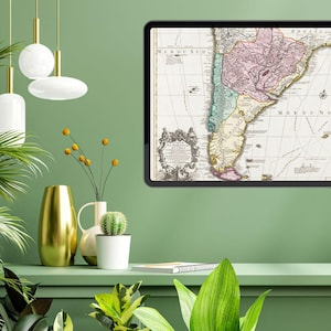 Może przedstawiać: Antyczna mapa Ameryki Południowej, oprawiona w czarną ramę, wisi na zielonej ścianie. Mapa jest w odcieniach brązu, różu i zieleni, z tekstem w języku hiszpańskim. Mapa jest otoczona złotą ramą.