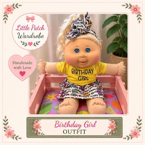 May include: A doll with blonde hair styled in a ponytail with a patterned headband, wearing a yellow t-shirt with the text BIRTHDAY GIRL and a skirt featuring a repeating Happy Birthday print, seated in a pink wooden crate with a colourful fruit pattern.