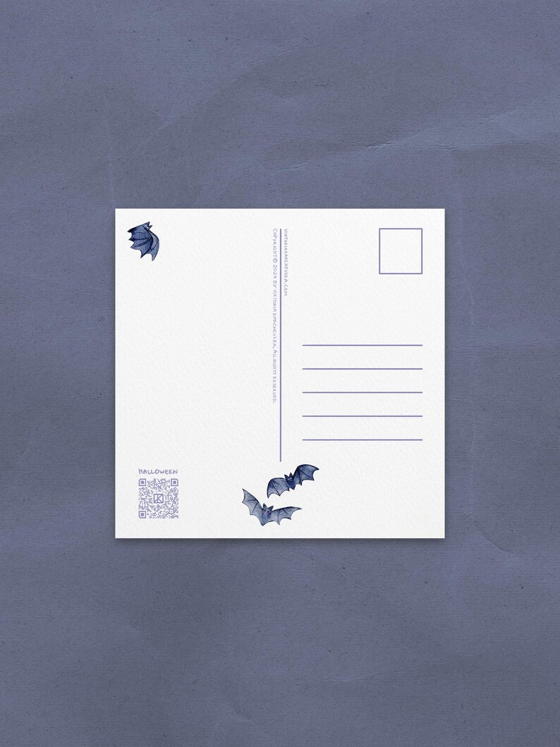 May include: White postcard with blue bat illustrations and the word "HALLOWEEN". The postcard has a QR code and lines for writing. The background is a textured, dark blue surface.