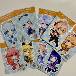 Op de afbeelding: Een set van tien Genshin Impact chibi-personage stickers. De stickers tonen verschillende personages uit de game, waaronder een meisje met blauw haar, een jongen met paars haar, een meisje met roze haar en een meisje met groen haar. De stickers zijn gedrukt op een witte achtergrond met een geruit patroon.