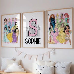 Könnte beinhalten: Drei gerahmte Drucke mit Disney-Prinzessinnen. Ein Druck zeigt den Buchstaben "S" und den Namen "SOPHIE". Die anderen beiden Drucke zeigen verschiedene Prinzessinnen in ihren Kleidern. Die Drucke befinden sich über einem weißen Aufbewahrungsschrank mit Kissen und einem Teddybären.