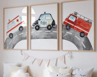 May include: Three framed watercolor prints of emergency vehicles: an ambulance, a police car, and a fire truck, each on a gray road. The prints are displayed above a wooden storage bench with pillows and a teddy bear.
