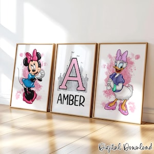 May include: Three framed prints featuring cartoon characters. One print shows Minnie Mouse in a blue dress, another displays the letter "A" with the name "AMBER", and the third features Daisy Duck. All prints have a pink watercolor background.