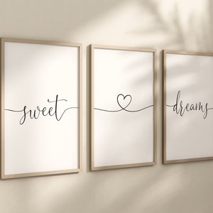 Pode incluir: Três impressões emolduradas com um design minimalista. As impressões apresentam as palavras "sweet" e "dreams" em escrita elegante, e um desenho de um coração. As molduras são de cor de madeira clara e o fundo é branco.