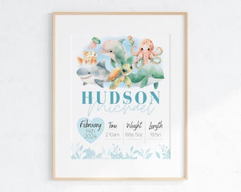 May include: A framed watercolor print featuring aquatic animals like a shark, dolphin, and octopus. The print includes the name "Hudson Michael" in blue, along with birth details: February 14th, 2024, 2:10 am, 6lbs 5oz, and 19.5in.