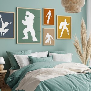May include: A bedroom scene with framed superhero art. The wall art features white silhouettes on colored backgrounds. The bed has teal bedding and white pillows. A woven lamp and side table are on the left.