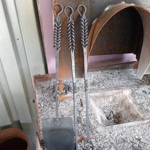 May include: A set of three fireplace tools with twisted metal handles. The tools include a poker, a shovel, and a set of tongs. The tools are sitting on a bed of ashes.