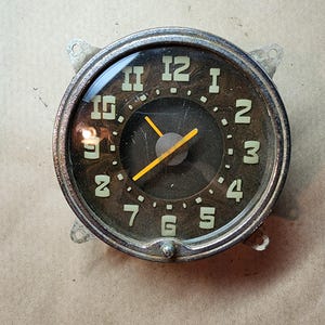 May include: A vintage clock face with black numbers and a silver frame. The clock hands are yellow and the face is black.