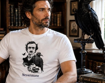 May include: A white short-sleeved t-shirt featuring a black graphic print of Edgar Allan Poe and a raven perched on a stack of books. Below the illustration, the word Nevermore is printed in a dark, serif font centered on the chest area.