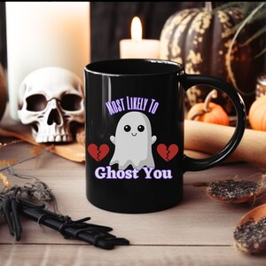 May include: Black coffee mug with a white ghost illustration and the text "Most Likely To Ghost You" in purple. Two broken red hearts are on either side of the ghost.