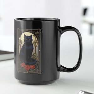 May include: Black ceramic coffee mug with a black cat illustration in an art nouveau style frame. The cat is sitting on a bed of red roses.